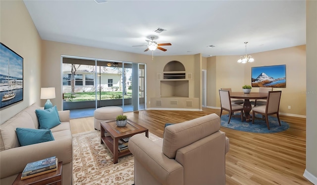 living room with light wood-type flooring, baseboards, visible vents, and ceiling fan with notable chandelier