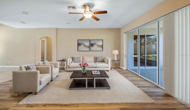 living room featuring baseboards, visible vents, arched walkways, ceiling fan, and wood finished floors