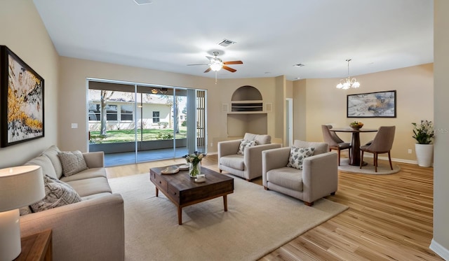 living room with light wood-type flooring, baseboards, visible vents, and ceiling fan with notable chandelier