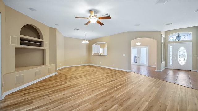 unfurnished living room featuring built in shelves, ceiling fan with notable chandelier, visible vents, baseboards, and light wood-style floors