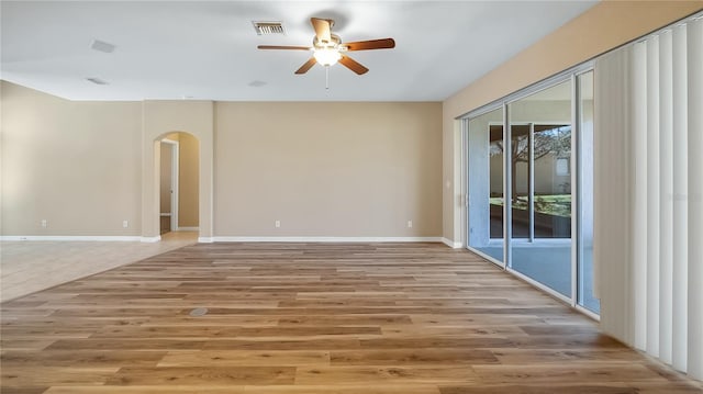 empty room featuring arched walkways, light wood finished floors, visible vents, a ceiling fan, and baseboards