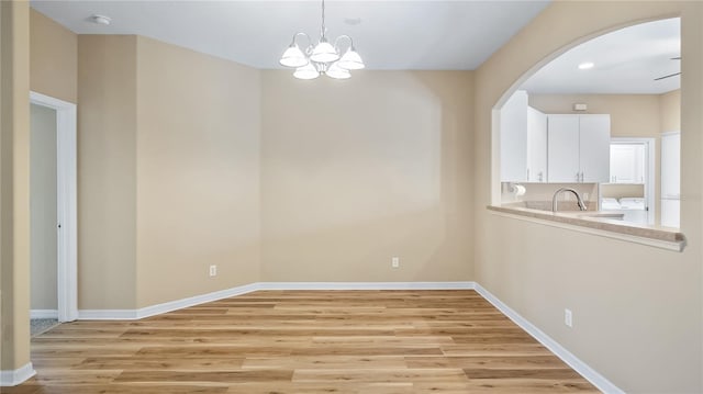 unfurnished dining area with light wood-style floors, arched walkways, a sink, and baseboards