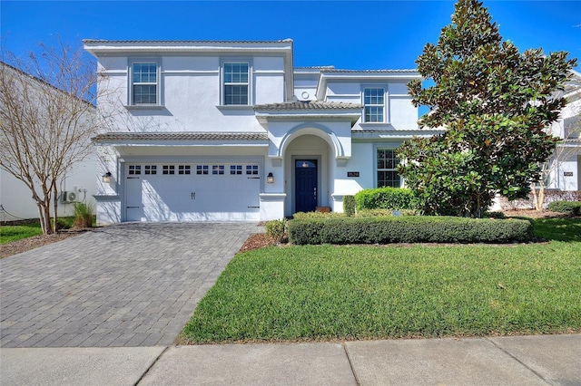 view of front facade featuring decorative driveway, an attached garage, a front yard, and stucco siding