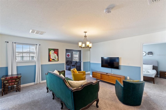 living room with a textured ceiling, carpet floors, visible vents, and a notable chandelier