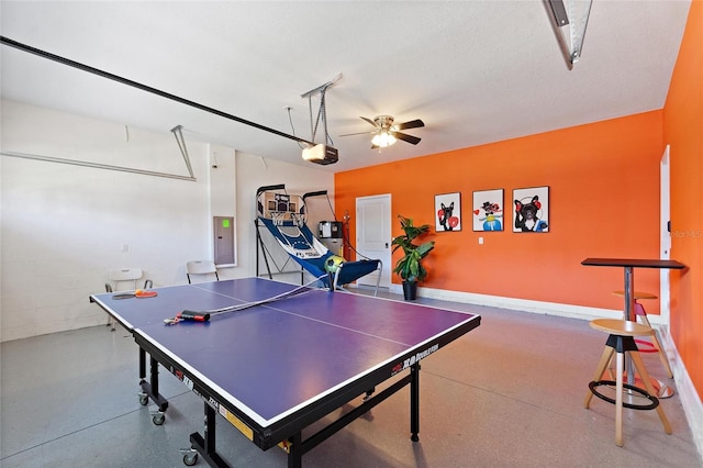 rec room with ceiling fan, a garage, speckled floor, electric panel, and concrete block wall