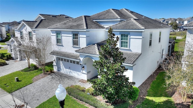 view of front of home with decorative driveway, an attached garage, a tile roof, and stucco siding