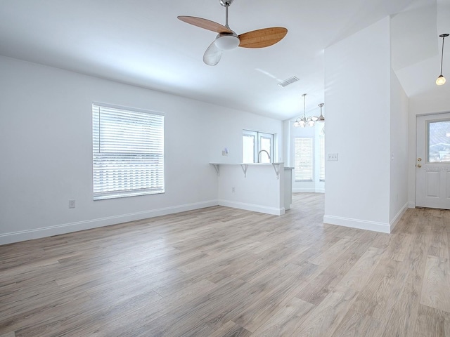 unfurnished living room with baseboards, visible vents, vaulted ceiling, ceiling fan with notable chandelier, and light wood-type flooring