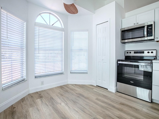 kitchen featuring light wood-type flooring, stainless steel appliances, white cabinets, baseboards, and ceiling fan