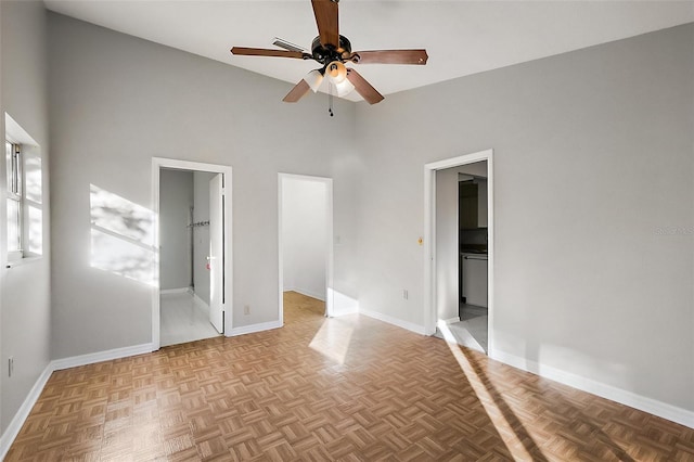 unfurnished bedroom featuring ensuite bathroom, a high ceiling, a ceiling fan, baseboards, and a walk in closet