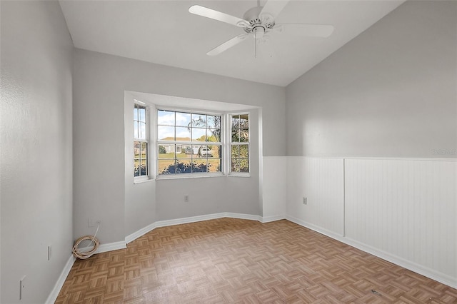 unfurnished room with a wainscoted wall, vaulted ceiling, a ceiling fan, and baseboards