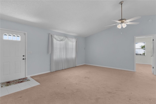 tiled foyer entrance featuring vaulted ceiling, a textured ceiling, a ceiling fan, and carpet floors