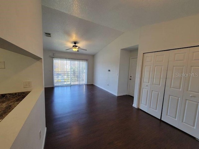 unfurnished living room with a textured ceiling, visible vents, a ceiling fan, vaulted ceiling, and dark wood-style floors