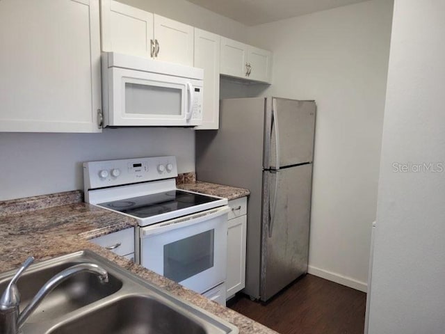 kitchen featuring dark wood-type flooring, white cabinets, a sink, white appliances, and baseboards