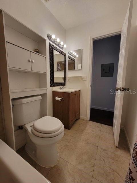 bathroom featuring toilet, vanity, electric panel, baseboards, and tile patterned floors