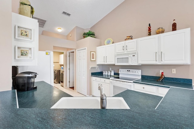 kitchen featuring dark countertops, white cabinetry, a sink, separate washer and dryer, and white appliances