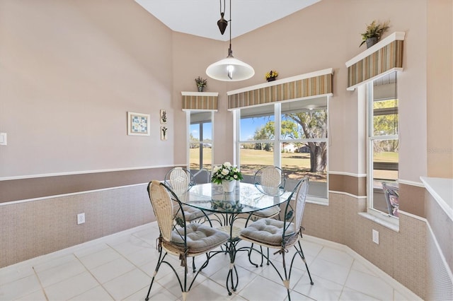 tiled dining room featuring wainscoting, a towering ceiling, and a wealth of natural light