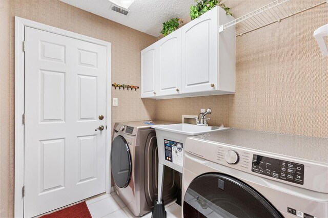 washroom featuring washer and clothes dryer, visible vents, cabinet space, light tile patterned flooring, and a textured ceiling