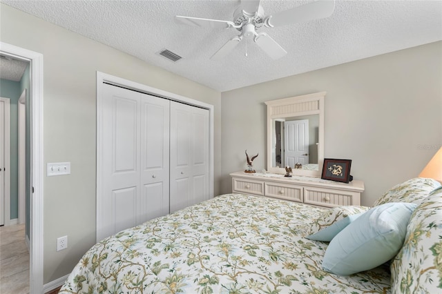 bedroom featuring ceiling fan, a textured ceiling, visible vents, and a closet