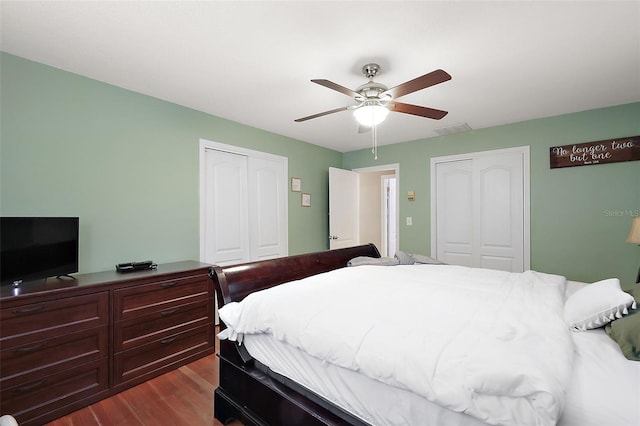 bedroom featuring a ceiling fan, visible vents, dark wood-type flooring, and two closets