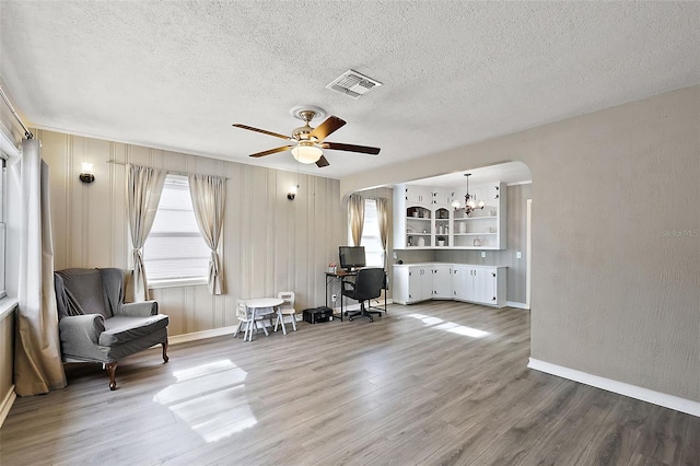 living area with arched walkways, a textured ceiling, wood finished floors, and visible vents