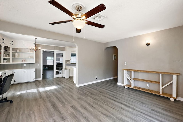 unfurnished living room with arched walkways, visible vents, baseboards, and wood finished floors