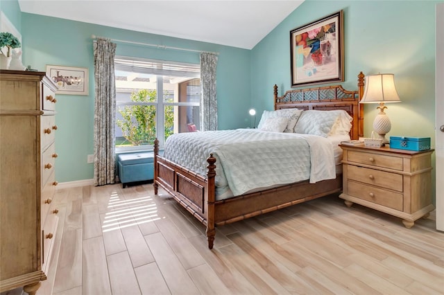 bedroom with vaulted ceiling, light wood-style floors, and baseboards