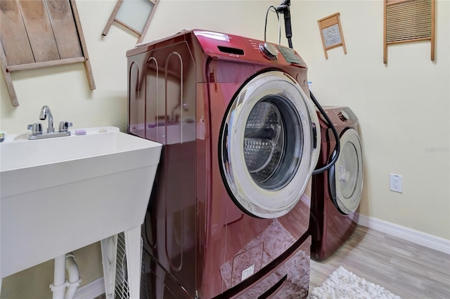 washroom featuring baseboards, laundry area, light wood-style floors, independent washer and dryer, and a sink