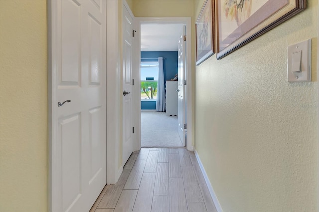 corridor featuring wood finish floors, baseboards, and a textured wall