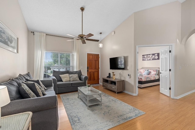 living area featuring high vaulted ceiling, light wood-type flooring, and baseboards