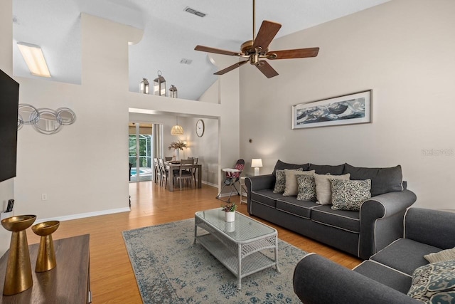 living room featuring high vaulted ceiling, wood finished floors, a ceiling fan, visible vents, and baseboards