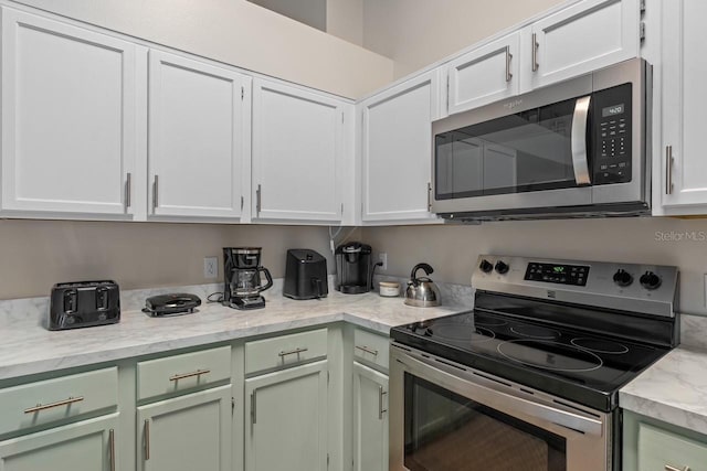 kitchen featuring stainless steel appliances, white cabinetry, and light stone counters