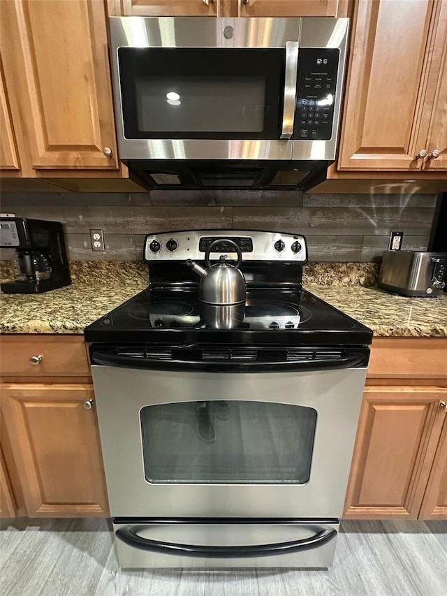 kitchen featuring light stone countertops, stainless steel appliances, backsplash, and brown cabinetry