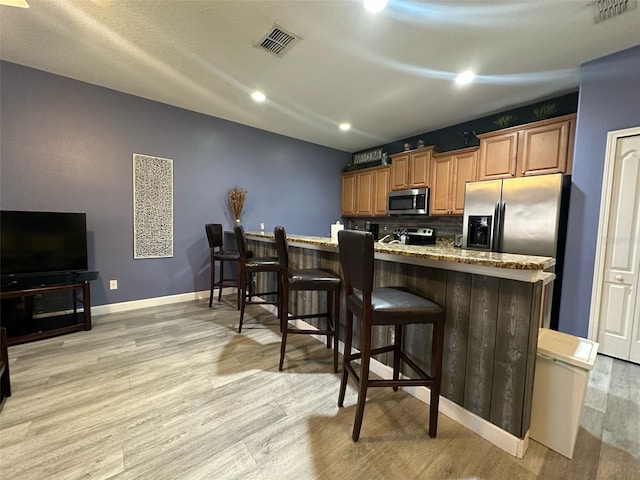 kitchen with appliances with stainless steel finishes, light wood-style floors, visible vents, and a kitchen breakfast bar