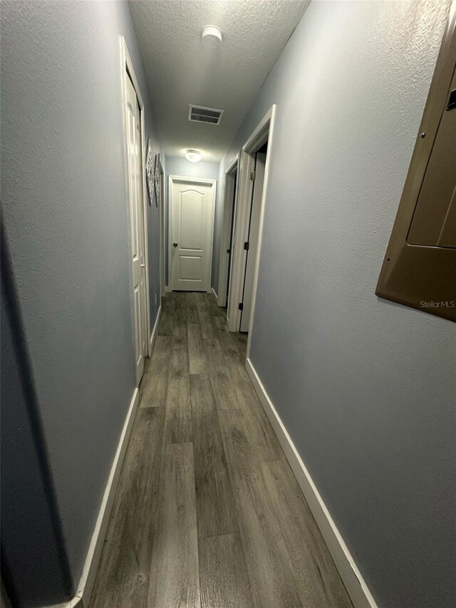 hallway with visible vents, dark wood finished floors, a textured ceiling, and baseboards