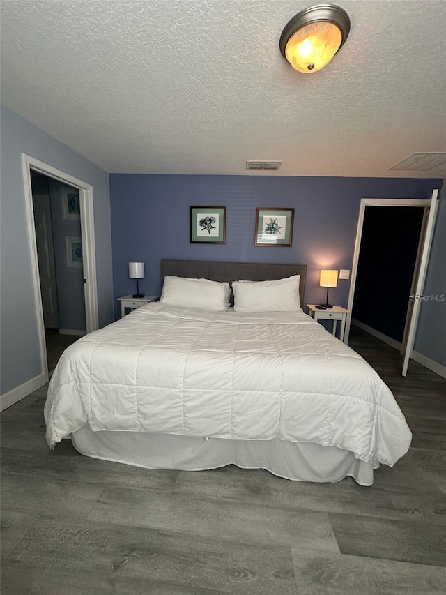 bedroom featuring a textured ceiling, wood finished floors, visible vents, and baseboards