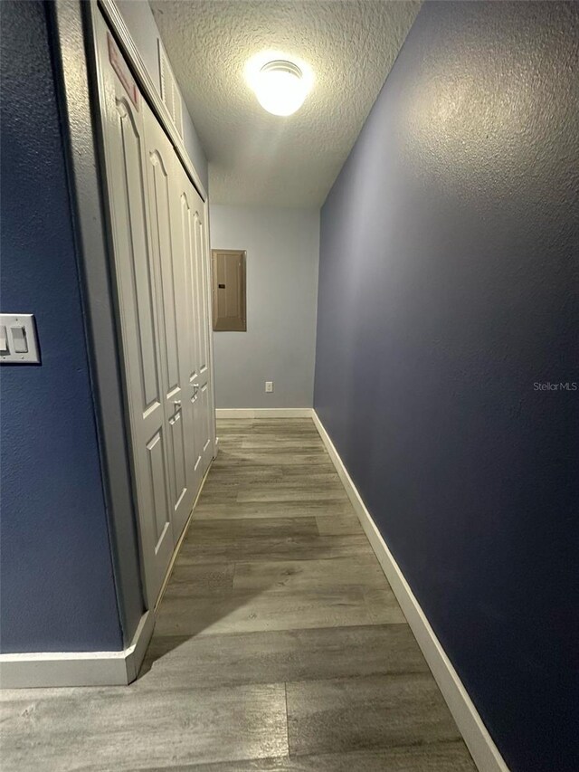 corridor featuring electric panel, a textured ceiling, baseboards, and wood finished floors