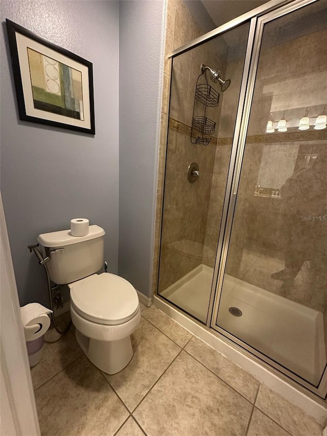 bathroom featuring toilet, a shower stall, baseboards, and tile patterned flooring