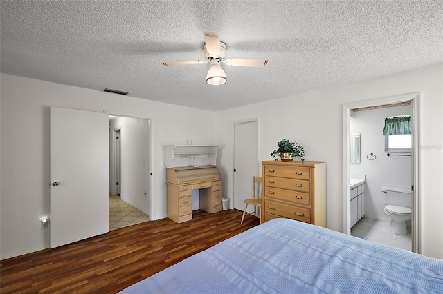 bedroom with visible vents, ceiling fan, a textured ceiling, ensuite bath, and wood finished floors