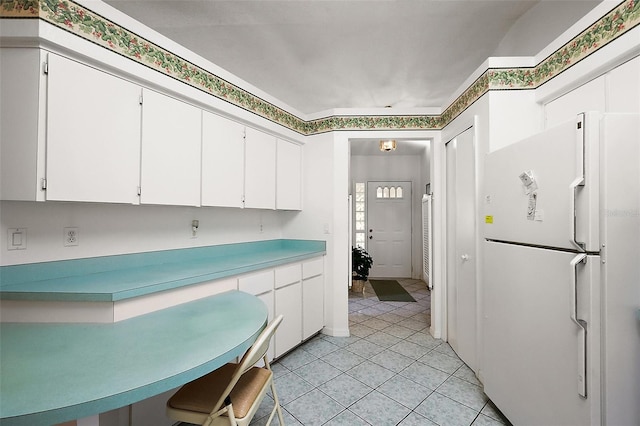 kitchen with light tile patterned flooring, white cabinets, light countertops, and freestanding refrigerator