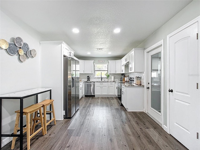 kitchen with decorative backsplash, white cabinets, stainless steel appliances, and dark wood-style flooring