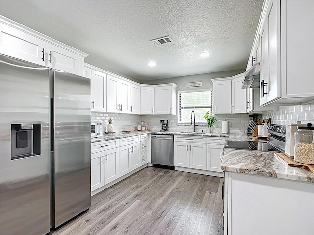 kitchen with visible vents, a sink, stainless steel appliances, light wood-style floors, and extractor fan