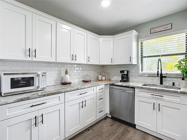 kitchen with a sink, tasteful backsplash, stainless steel dishwasher, dark wood finished floors, and white cabinets