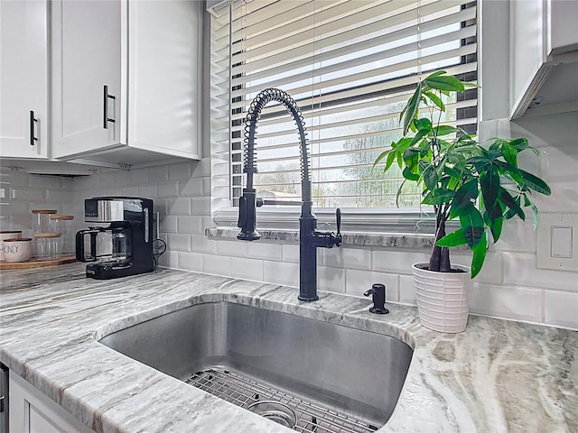 interior details featuring tasteful backsplash, light stone countertops, white cabinetry, and a sink