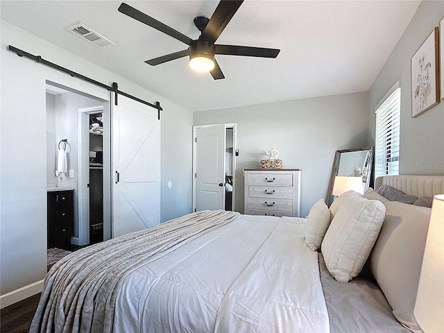 bedroom featuring visible vents, baseboards, a barn door, wood finished floors, and a ceiling fan