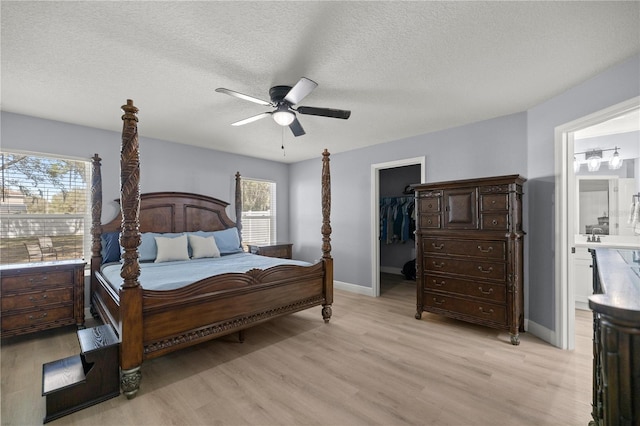 bedroom with light wood-style floors, a walk in closet, connected bathroom, and a textured ceiling