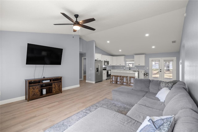 living room with lofted ceiling, ceiling fan, light wood-style flooring, and baseboards