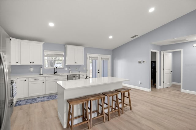 kitchen featuring a breakfast bar area, stainless steel appliances, a sink, white cabinets, and vaulted ceiling