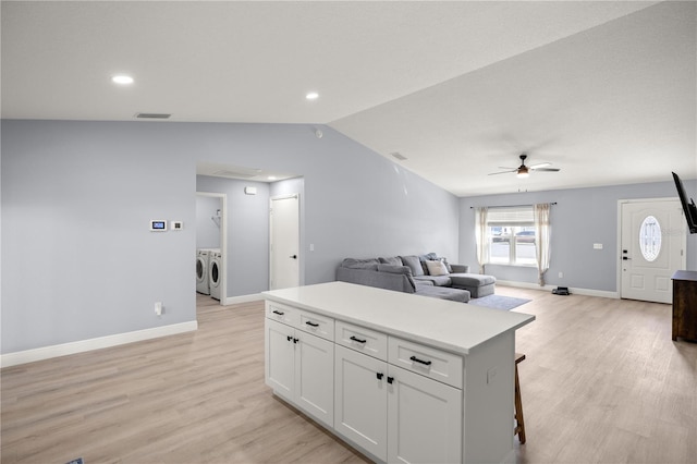 kitchen featuring vaulted ceiling, washer and clothes dryer, visible vents, and light wood-style floors