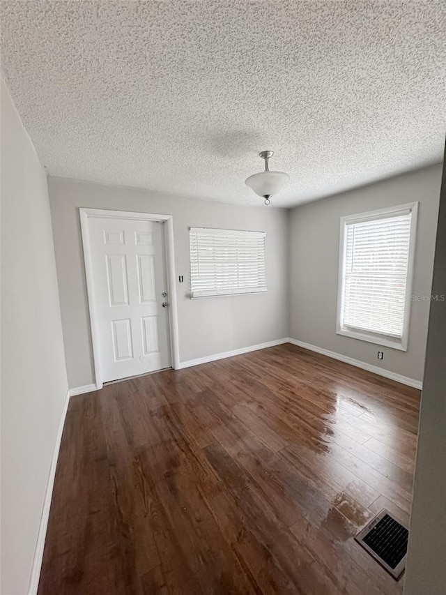 interior space with a textured ceiling, wood finished floors, visible vents, and baseboards