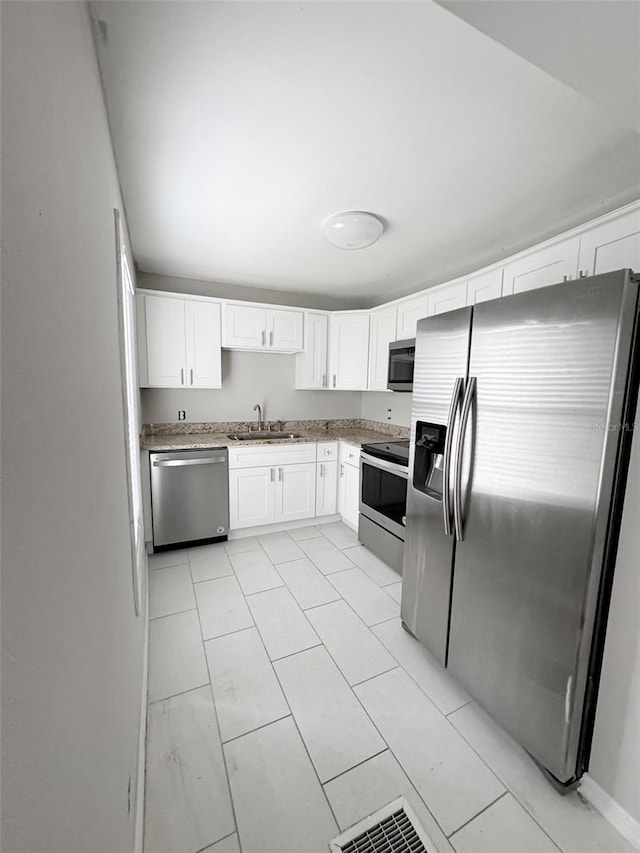 kitchen featuring stainless steel appliances, a sink, white cabinetry, and light stone countertops